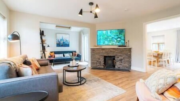 A spacious living room with a stone fireplace, a flat-screen TV mounted above it, and a modern sofa set.