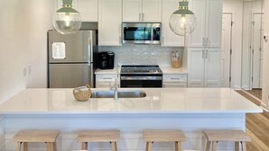 A modern kitchen with white cabinetry, stainless steel appliances, and a central island with bar stools. - Prime 30A Location/EZ Beach Access/Quiet Pool/Fast Wifi  (Santa Rosa Beach)