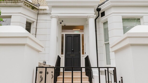 Una casa adosada con puerta delantera negra, escalones color beige y fachada blanca.