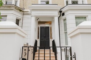 A townhouse with a black front door, beige steps, and a white exterior.