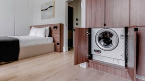 Habitación de hotel con cama, lavadora integrada en los muebles y puerta que da a otra habitación.