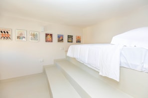 A bedroom with a bed, white walls, and a staircase.
