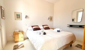 A hotel room with a bed, bedside tables, a mirror, and a wall-mounted shelf.