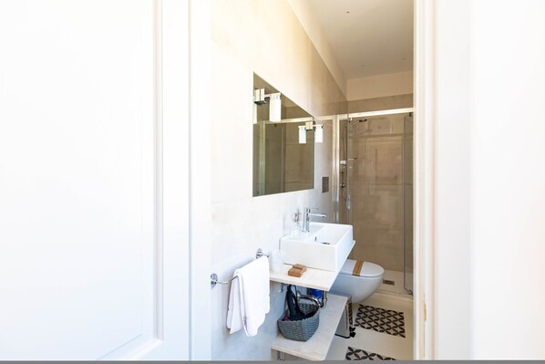 Uma casa de banho moderna com uma pia branca, espelho e chuveiro.