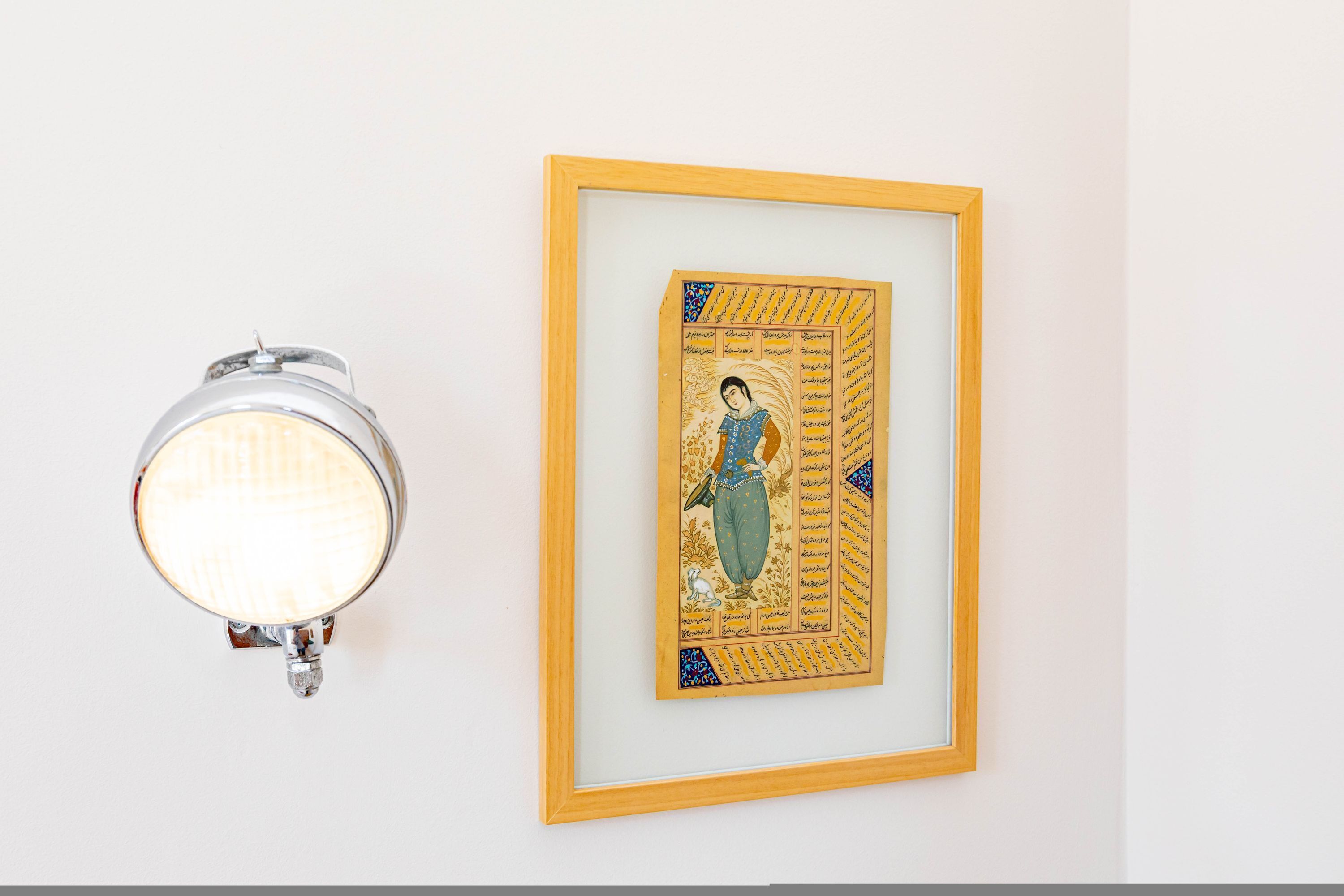 Uma obra de arte emoldurada com uma pessoa e texto, e uma luminária fixada na parede.