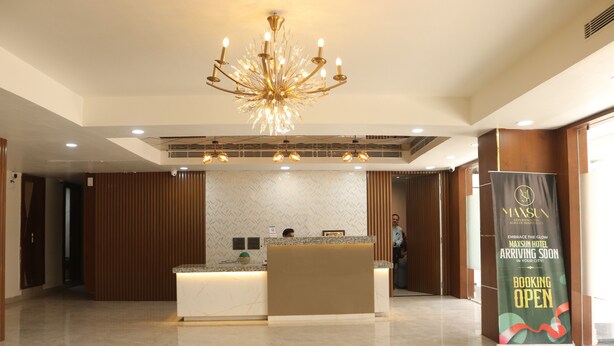 A hotel reception area with a modern chandelier, a reception desk, and a banner advertising the hotel's arrival. - Hotel Maxsun Gwalior (Gwalior)