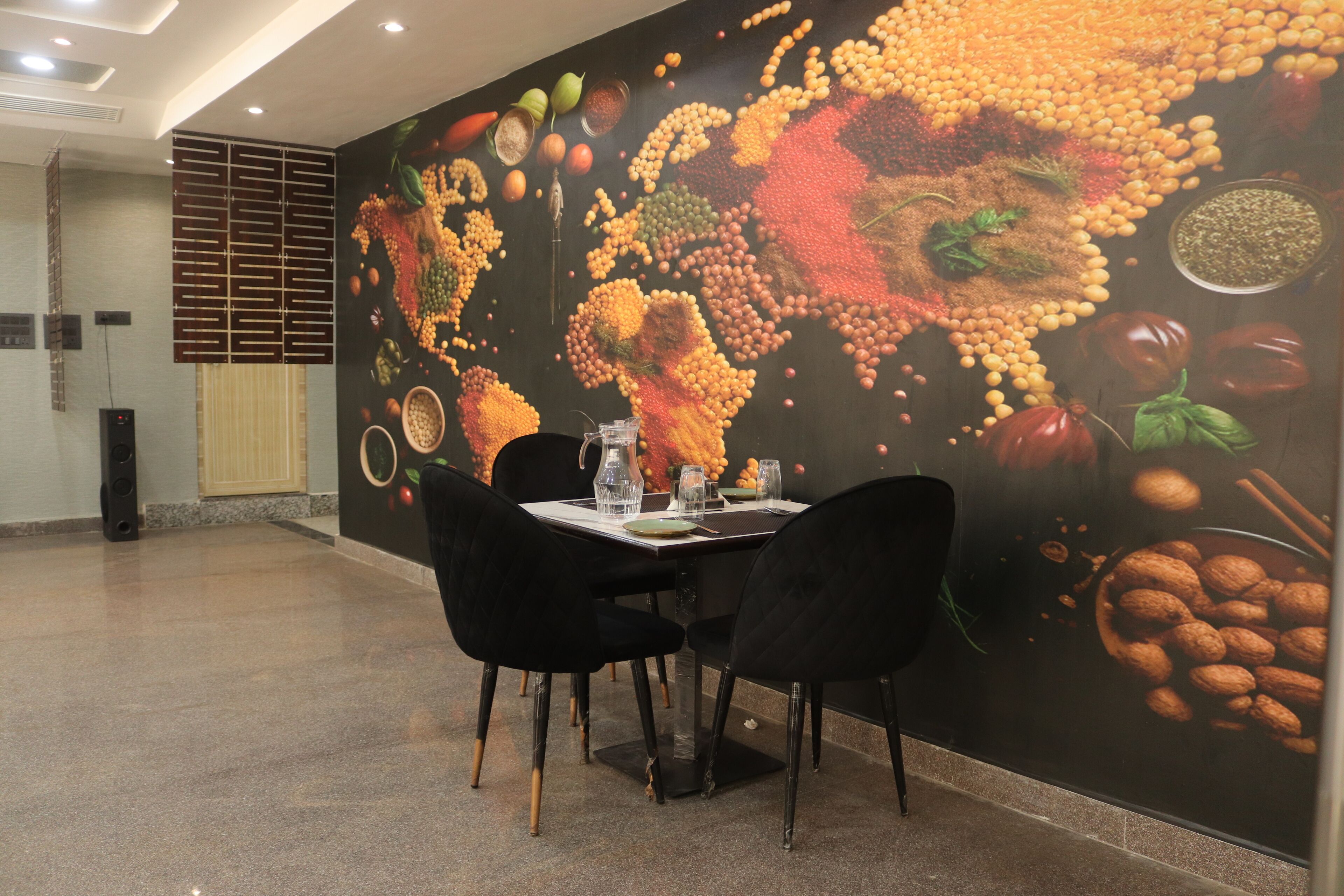 A dining area with a wall mural of various fruits and vegetables, a table set with plates, glasses, and black chairs.