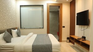 A modern bedroom with a large bed, a TV mounted on the wall, and a wooden bench beside the bed. - Hotel Maxsun Gwalior (Gwalior)