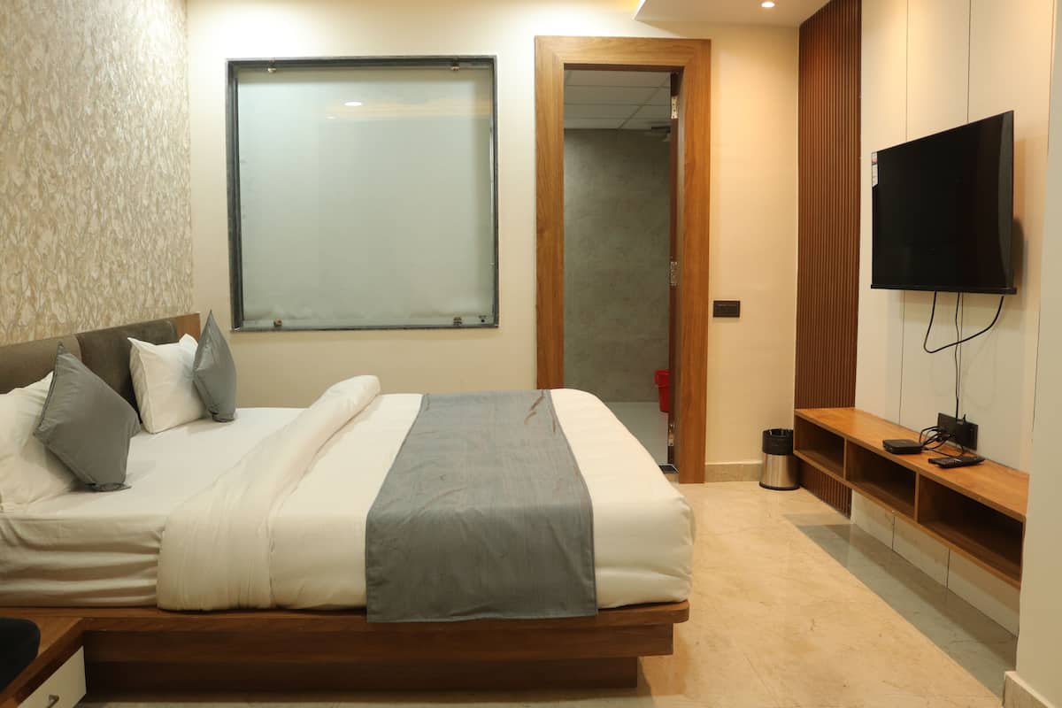 A modern bedroom with a large bed, a TV mounted on the wall, and a wooden bench beside the bed.