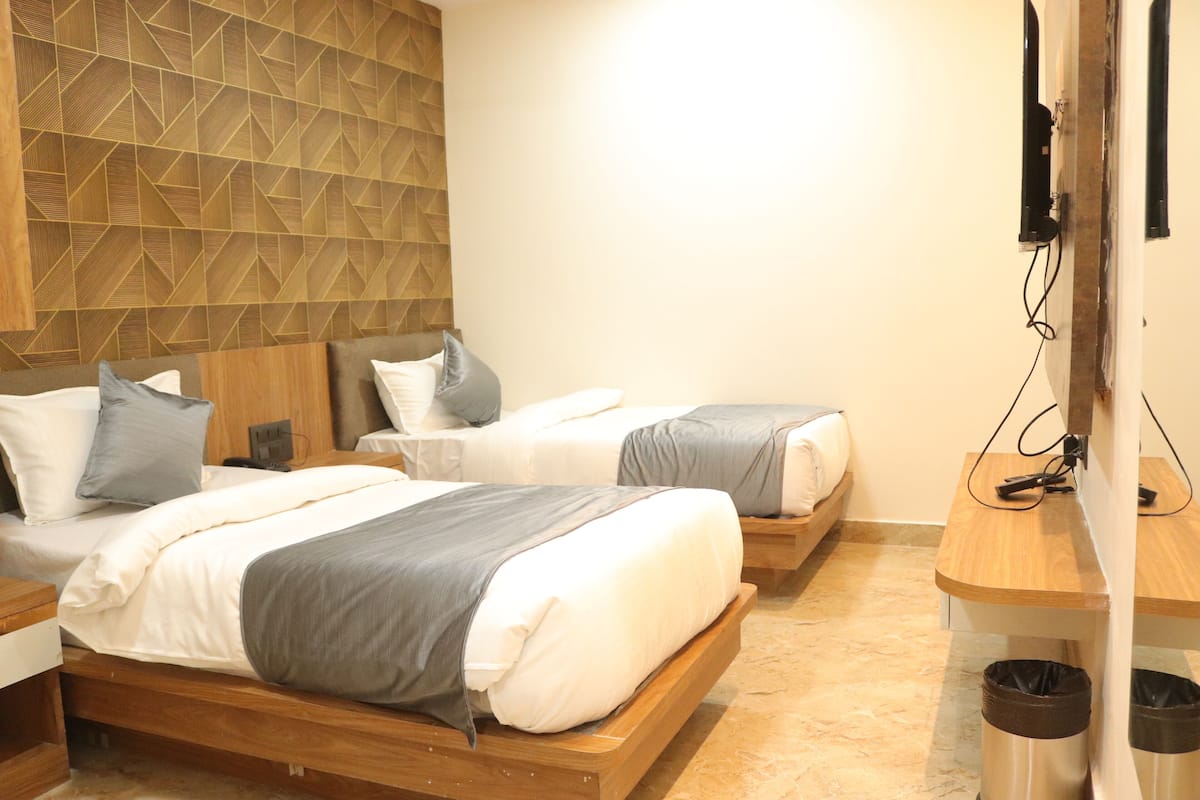 A hotel room with two beds, a wooden headboard, a wooden desk, and a trash bin.