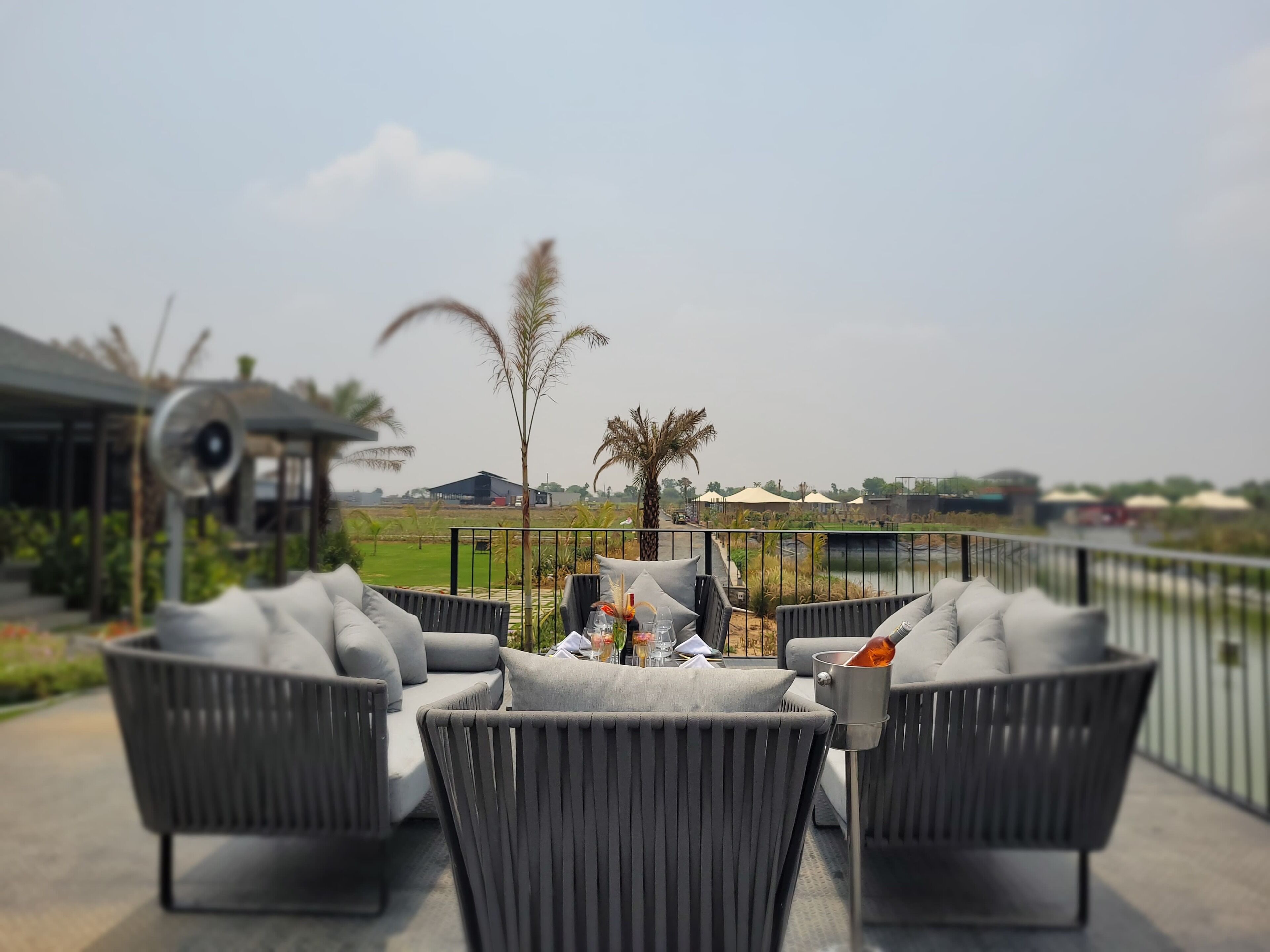 A seating area with grey upholstered chairs and a table, overlooking a landscaped garden and a body of water.