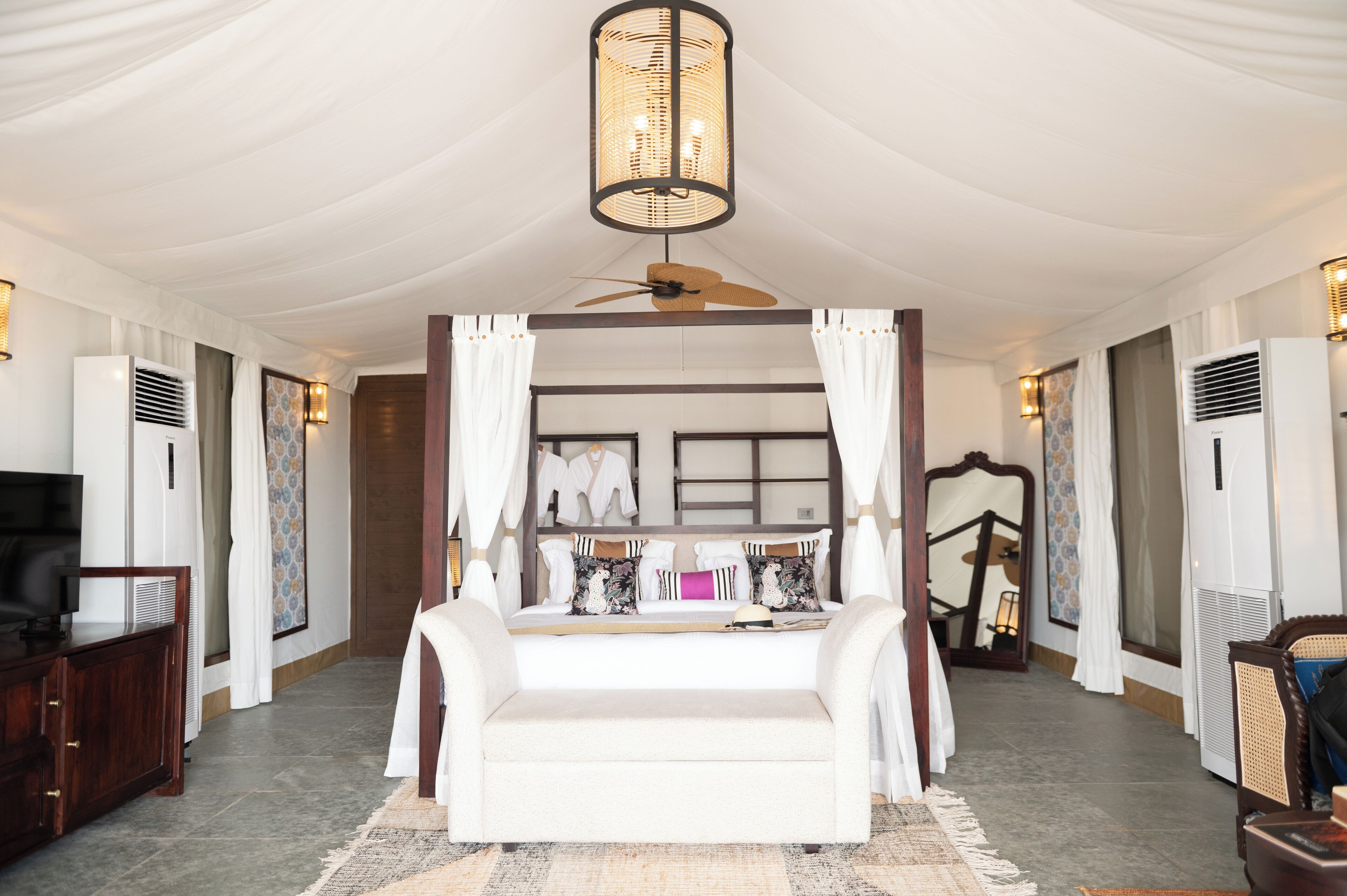 A spacious bedroom with a large bed, a ceiling fan, and a large mirror. There is a TV and a wooden dresser in the room.