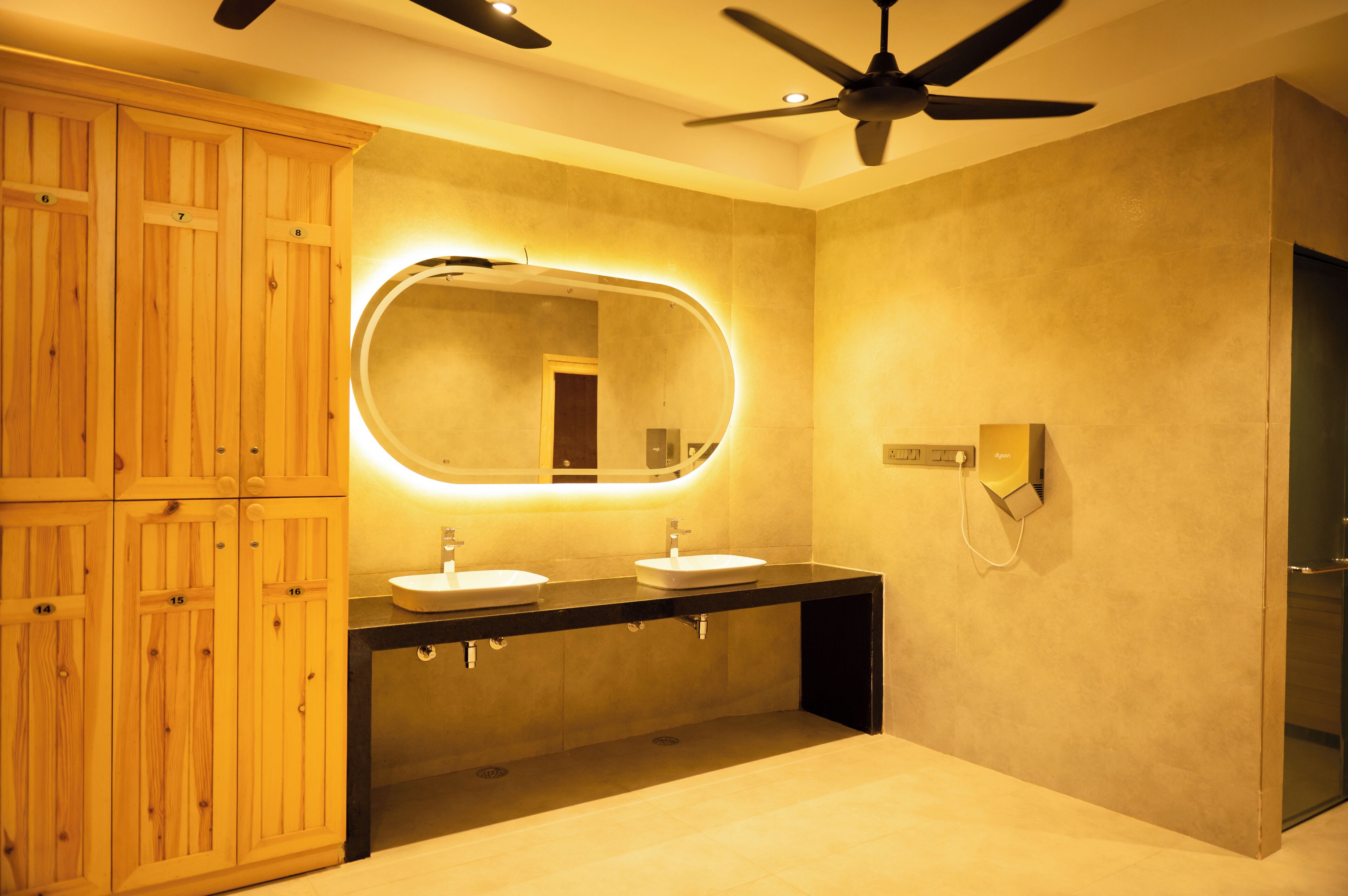 Un baño moderno con armarios de madera, un espejo grande, dos lavamanos y un ventilador de techo.