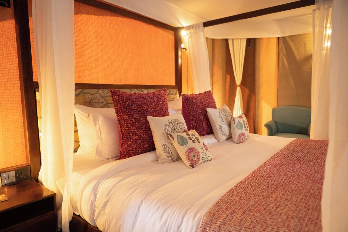 Ein Hotelzimmer mit einem großen Bett, mehreren Kissen, einem Nachttisch und einem Sessel.