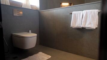 Une salle de bain moderne comprenant des toilettes, un porte-serviettes avec deux serviettes, un luminaire et un petit tapis.