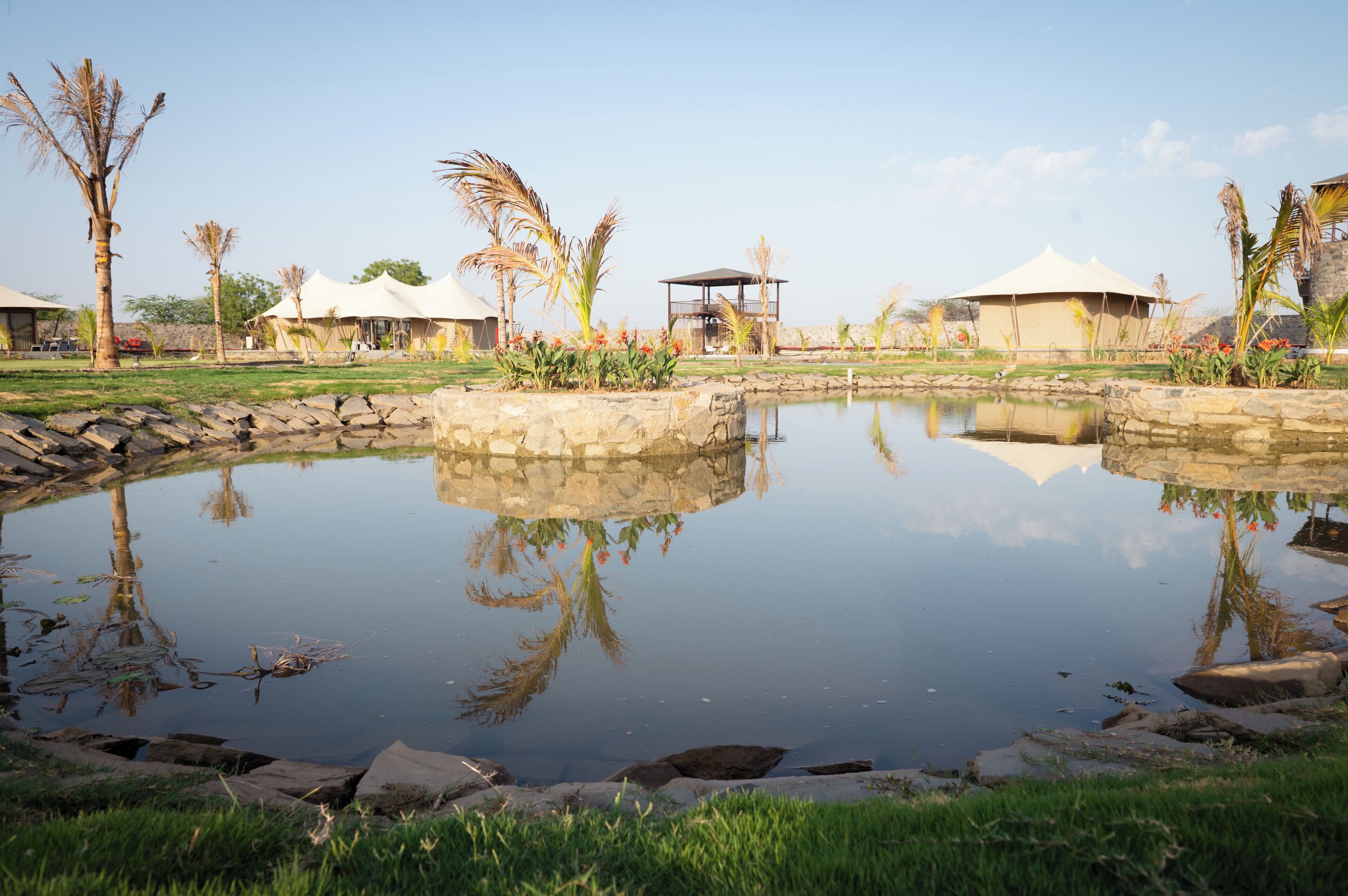 A serene outdoor setting with a pond, stone walls, and several tents.