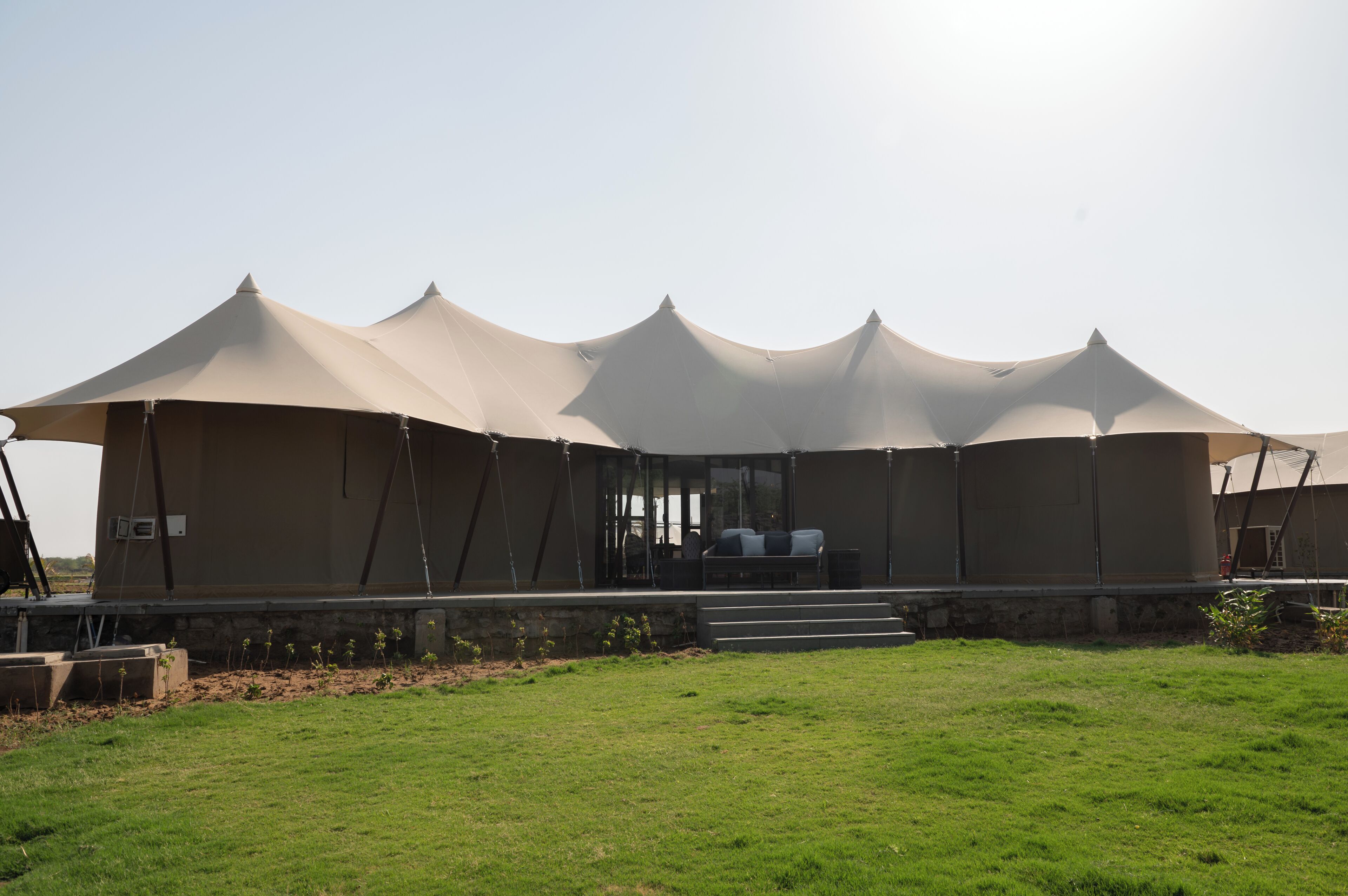 A series of large tents with a covered seating area in the center, surrounded by a grassy field.
