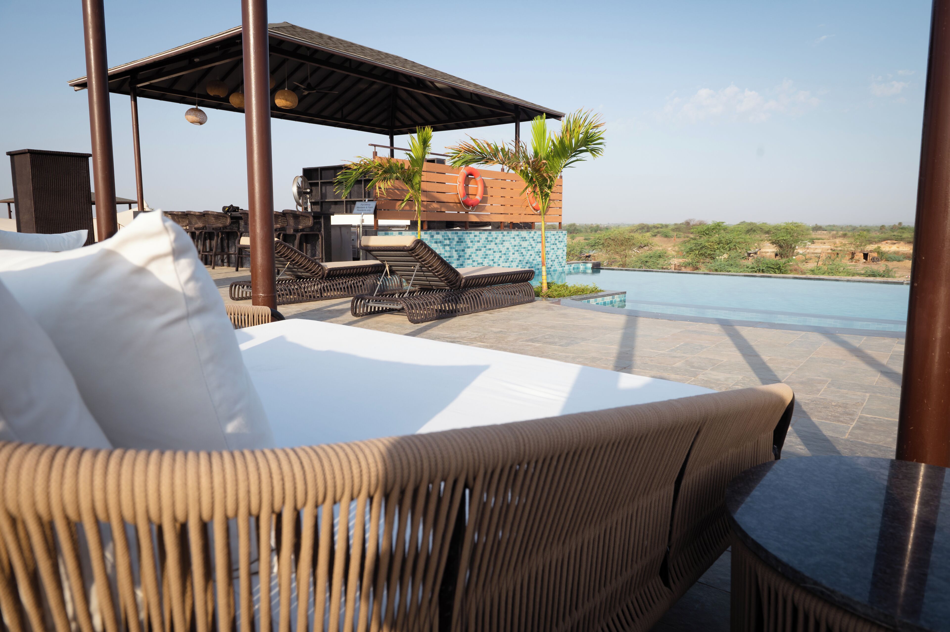 A poolside area with wicker furniture, a covered seating area, and a view of the pool and landscape.