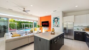 A modern kitchen with a central island, white cabinets, and a large TV screen displaying 'NETFLIX'. - Modernism week gem STR 003734 (Palm Springs)