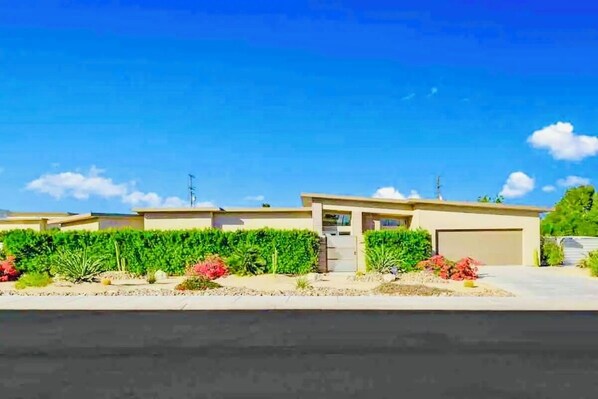 A modern two-story house with a garage, surrounded by well-maintained landscaping and a clear blue sky.