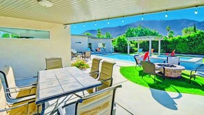 An outdoor patio with a table and chairs, a fire pit, and a pool. - Modernism week gem STR 003734 (Palm Springs)