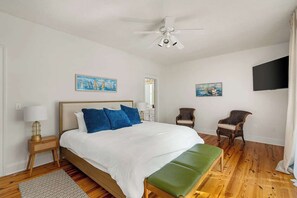 Une chambre à coucher comprenant un lit, un banc, deux chaises, un ventilateur de plafond et des œuvres d’art accrochées aux murs.