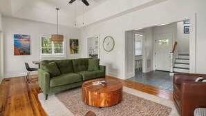 Ein geräumiges Wohnzimmer mit einem grünen Sofa, einem Holztisch und einem Deckenventilator.
