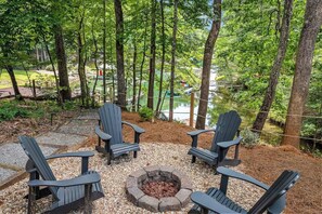 A forested outdoor seating area with Adirondack chairs and a fire pit.