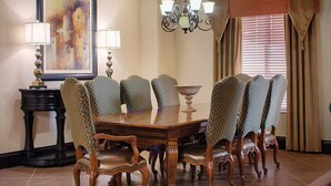 A formal dining room with a large wooden table surrounded by eight upholstered chairs, a chandelier, and a painting on the wall.
