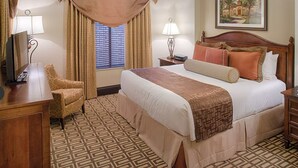 A hotel room with a large bed, a desk with a computer, a chair, and a window with curtains.