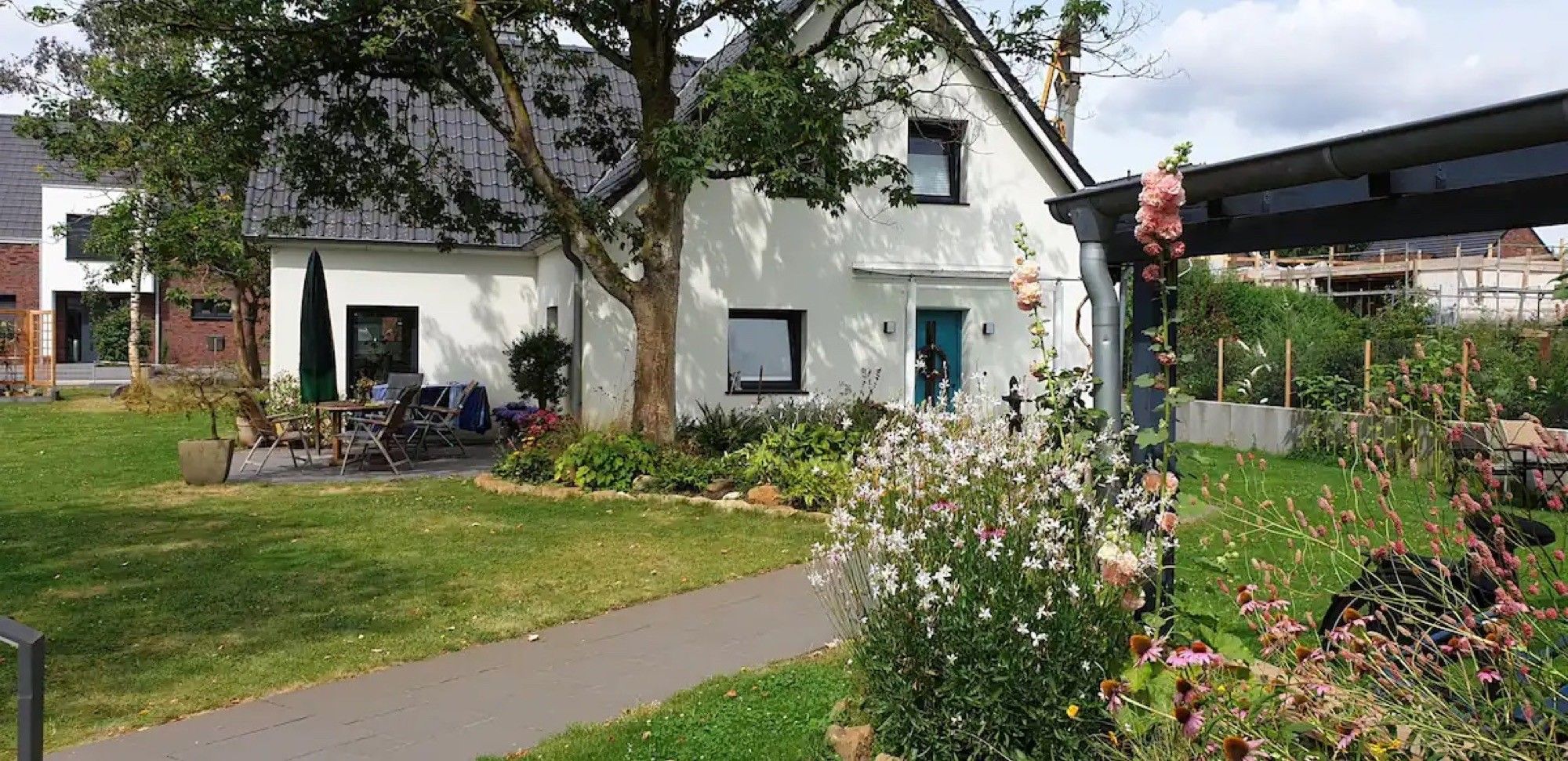 A white building with a green door, surrounded by a garden with various plants and flowers.