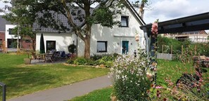 A white building with a green door, surrounded by a garden with various plants and flowers. - Apartment 'Ferienwohnung Feuerbach' with Shared Terrace, Shared Garden and Wi-Fi (Telgte)