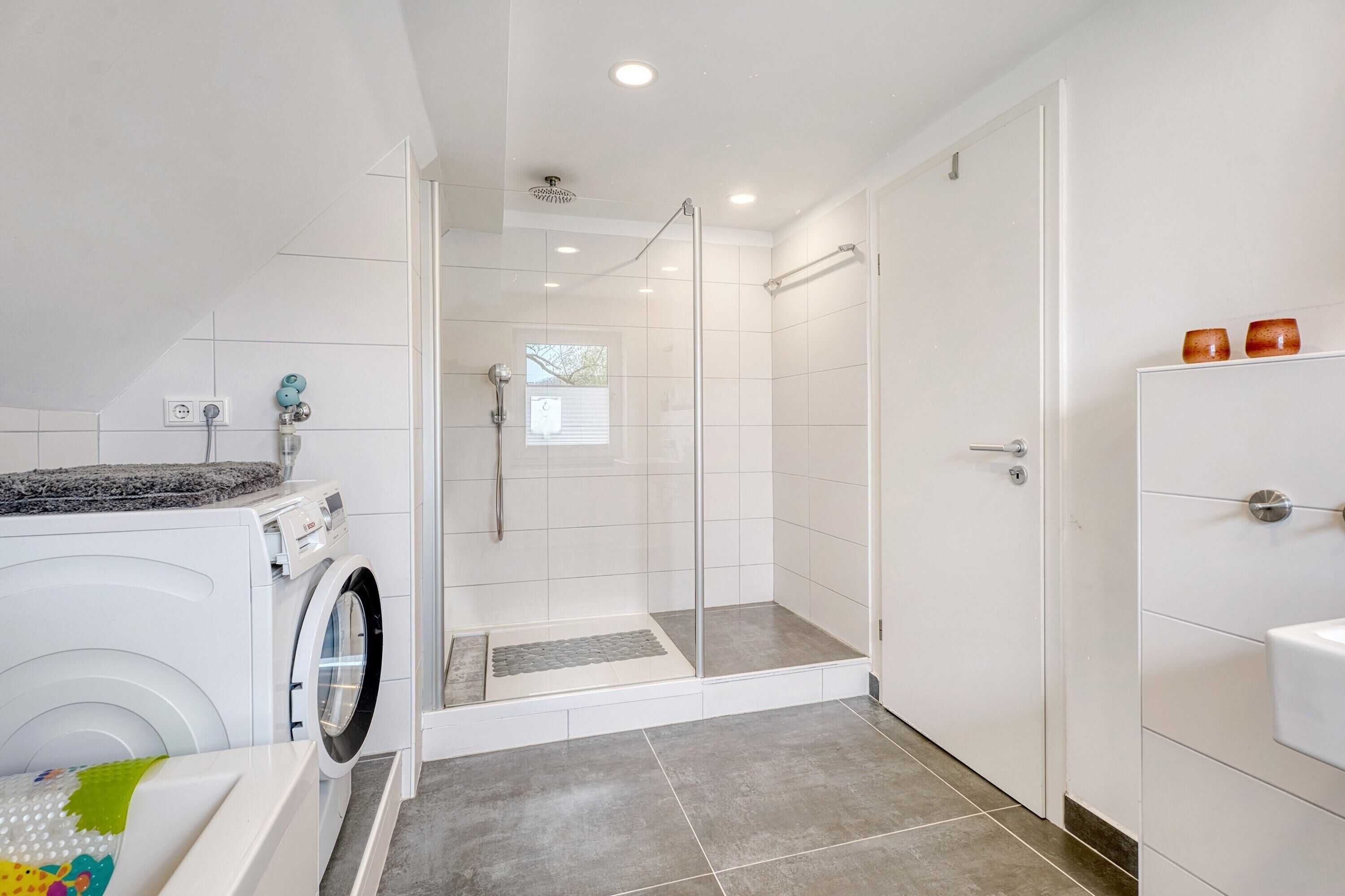 A modern bathroom with a glass-enclosed shower, a washing machine, and a sink.