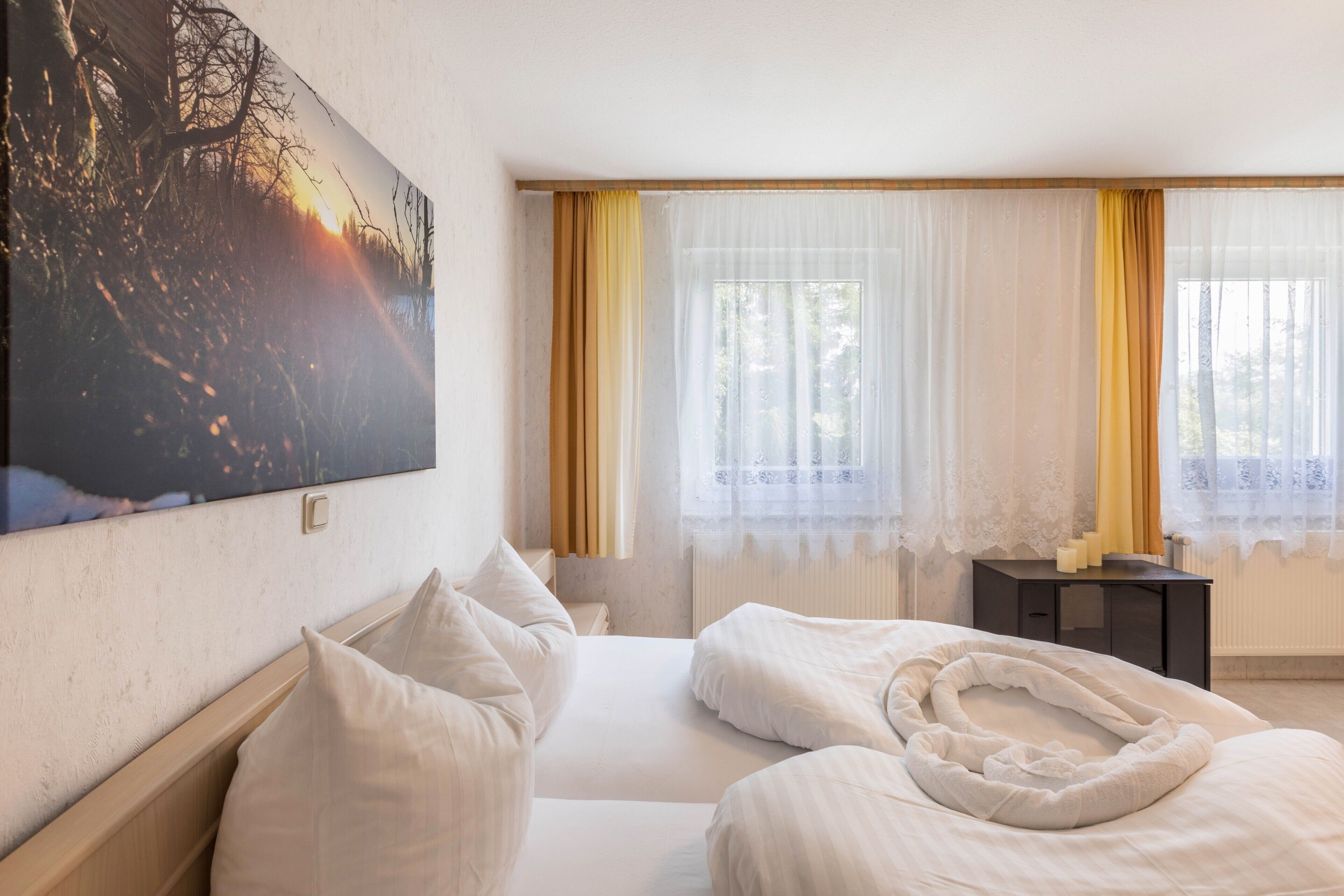 A hotel room with a bed, a bedside table, a painting on the wall, and a window with curtains.