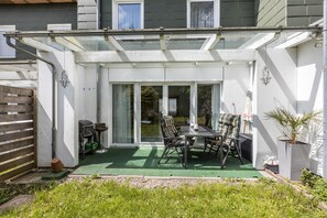 Eine überdachte Terrasse mit Tisch und Stühlen, einer Schiebetür und einem Belag aus grünem Kunstrasen.