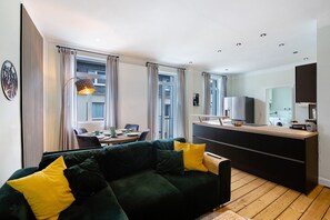 Una sala moderna con un sofá verde, un comedor y una cocina con estufa empotrada.