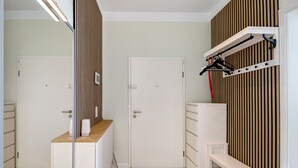 Una habitación con piso de madera, muebles blancos, un espejo y un tendedero de pared.