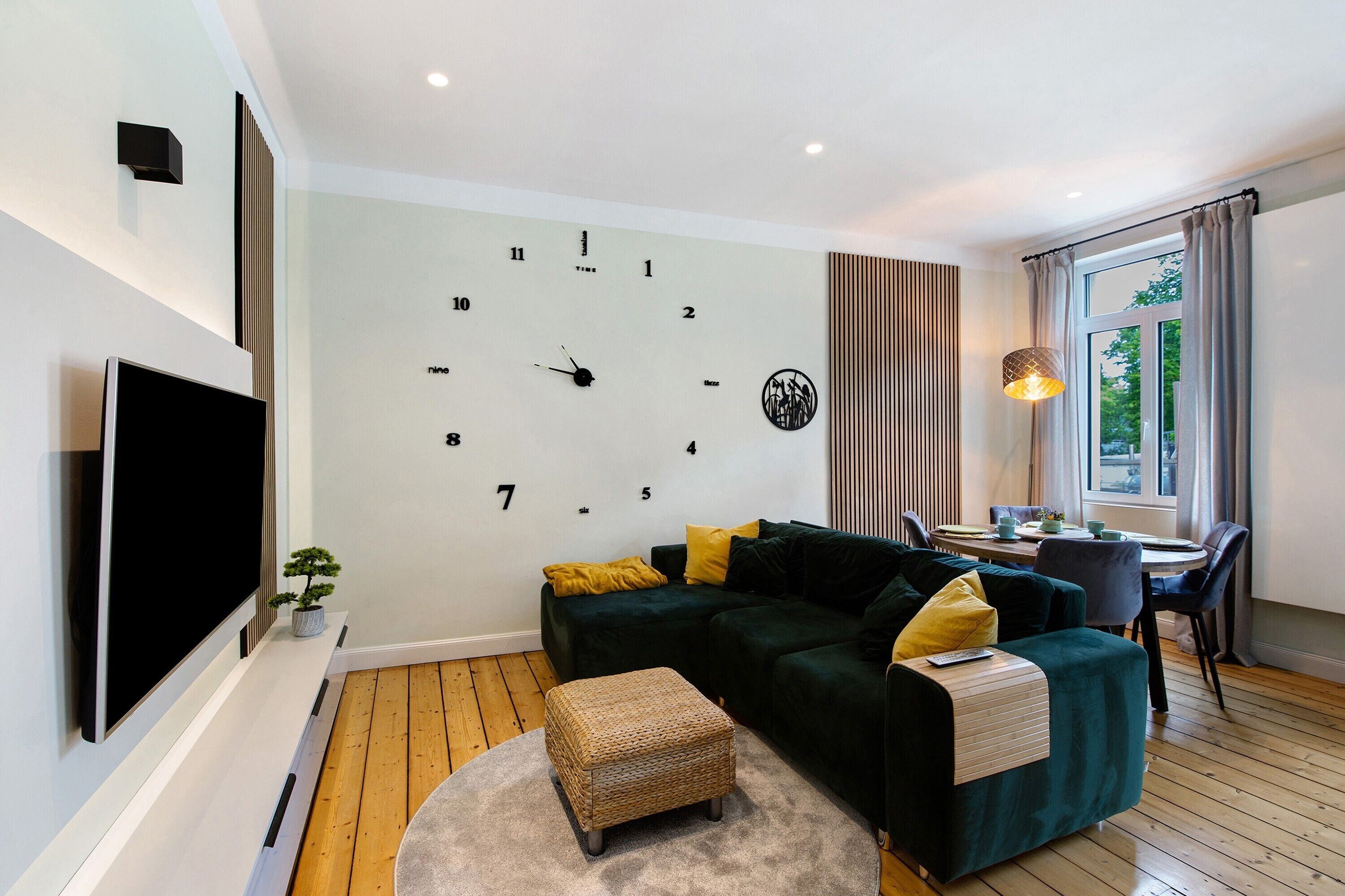 Ein modernes Wohnzimmer mit Flachbildfernseher, einem grünen Sofa, einem kleinen Tisch und einem Fenster mit Vorhängen.