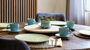 Una mesa de comedor dispuesta con platos, tazas y un centro de mesa.