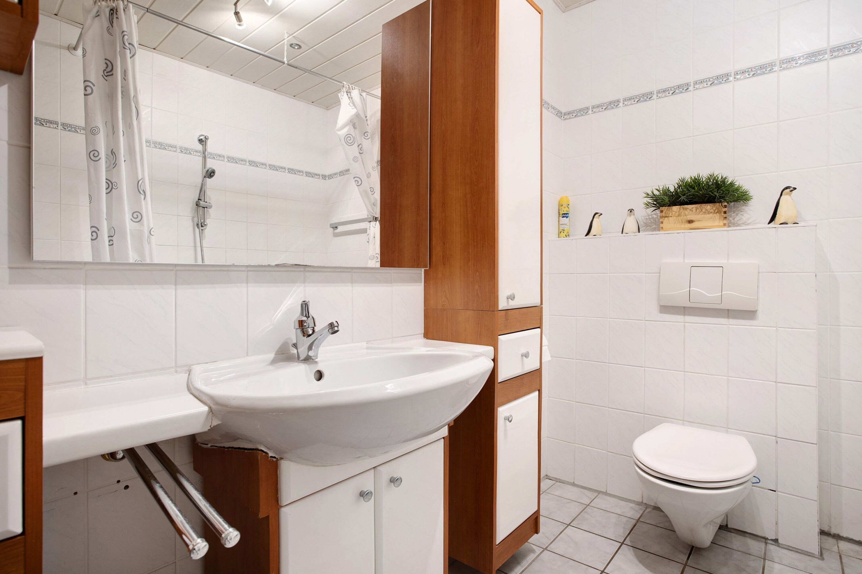 A bathroom with a white sink, wooden cabinet, white toilet, and a mirror.