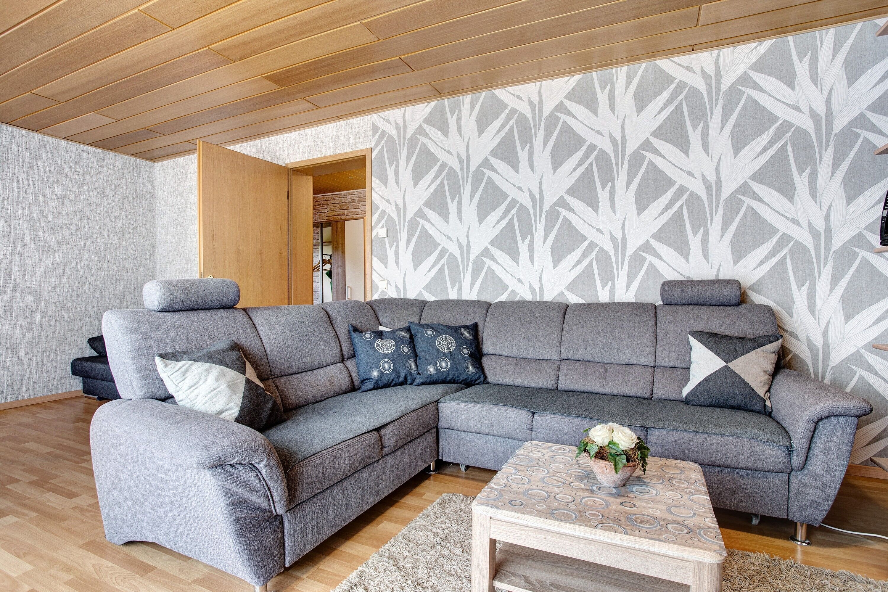 A modern living room with a sectional sofa, a wooden coffee table, and patterned wallpaper.