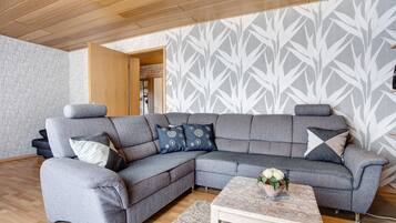 A modern living room with a sectional sofa, a wooden coffee table, and patterned wallpaper.