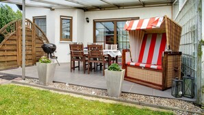 A covered patio area with a table and chairs, a wicker sofa, and a grill. - Apartment 'K Schröder' with Private Terrace, Private Garden and Wi-Fi (Sundhagen)