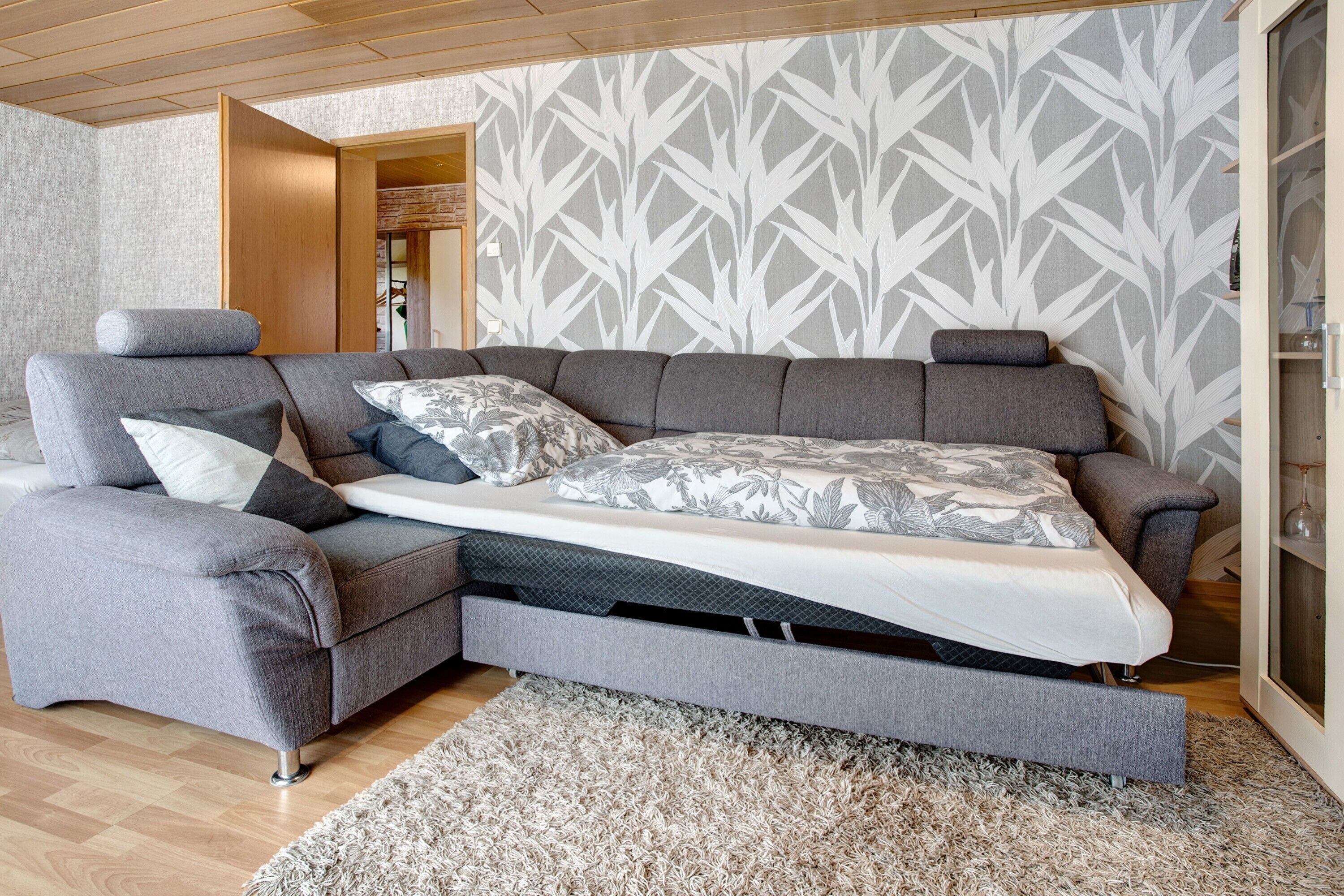 Una sala moderna con sofá cama, una puerta de madera y un papel tapiz estampado.
