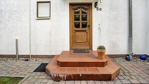 A white building with a wooden door, numbered 5a, and a small potted plant on the steps. - Apartment 'K Schröder' with Private Terrace, Private Garden and Wi-Fi (Sundhagen)