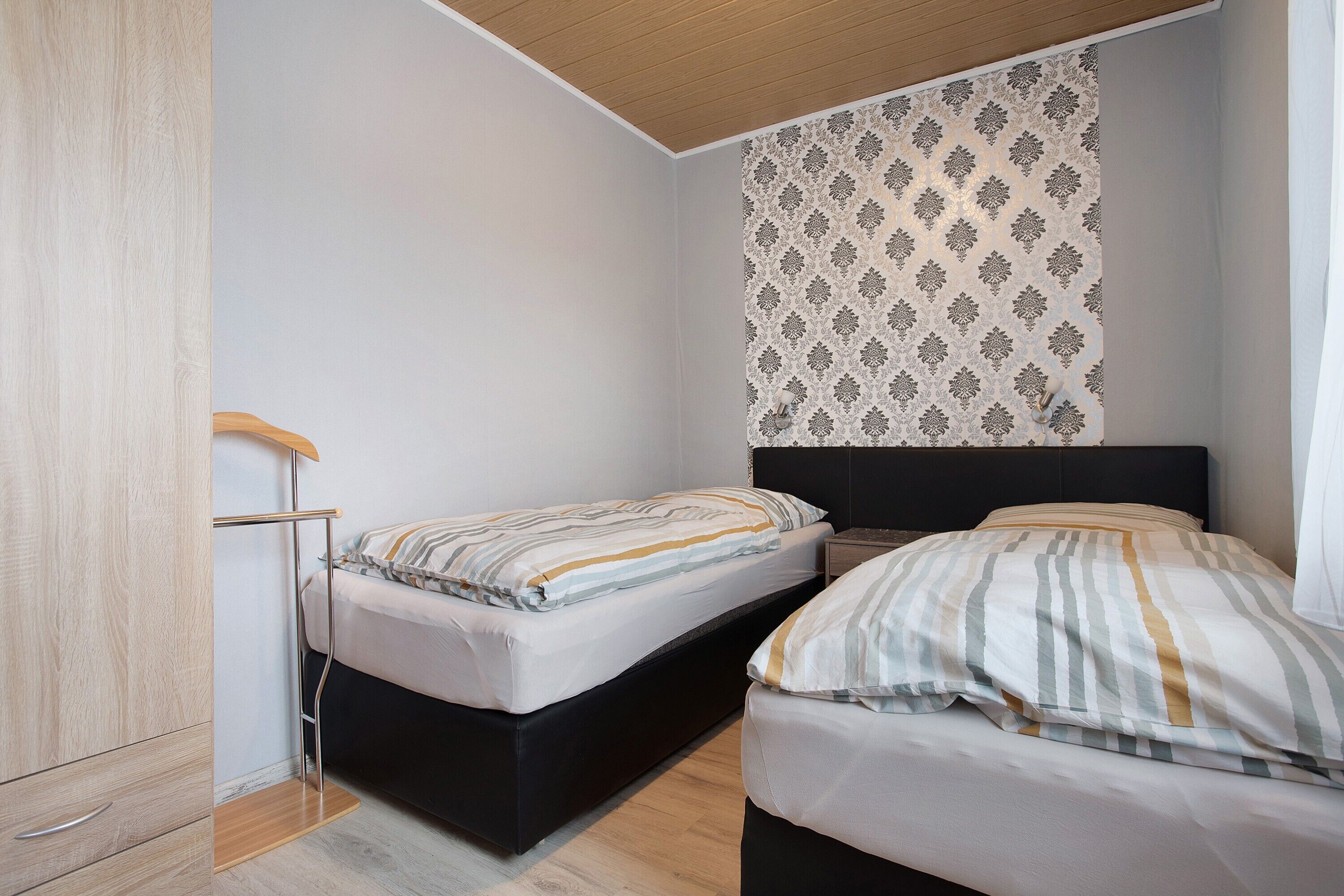 Een slaapkamer met twee bedden, een houten garderobe en behang met een patroon.