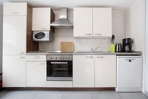 Una cucina moderna con mobili bianchi, forno a incasso, microonde, macchina da caffè e lavastoviglie.