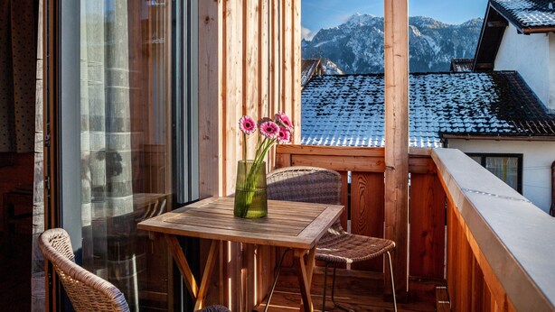 A wooden balcony with a table and chairs, a vase with flowers, and a view of snow-covered mountains. - Apartment 'Ferien Bei Mari' with Mountain View, Private Garden and Wi-Fi (Schwangau)