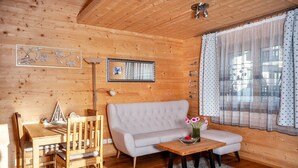 A wooden interior with a sofa, dining table, chairs, and a small table with flowers. - Apartment 'Ferien Bei Mari' with Mountain View, Private Garden and Wi-Fi (Schwangau)