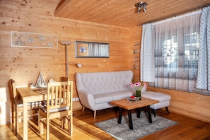 A wooden interior with a sofa, dining table, chairs, and a small table with flowers. - Apartment 'Ferien Bei Mari' with Mountain View, Private Garden and Wi-Fi (Schwangau)